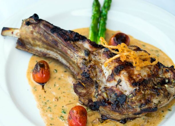 Grilled lamb chop served with creamy sauce, roasted cherry tomatoes, and asparagus